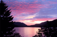 Pink and purple sky overlooking a mountain lake surrounded by trees and hills